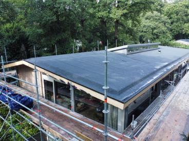 Exterieur van een woning waar dakrenovatie plaatsvindt, met ladders om het huis geplaatst