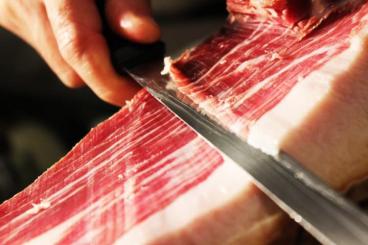 Slager Spijkenisse is bezig met het snijden van een groot stuk parmaham