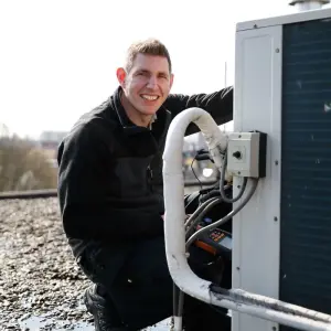 Een man in een zwart jasje werkt aan een airconditioner