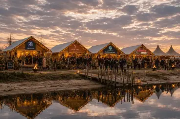 Bezoekers bij de verlichte winterfair-stands en vuurkorven aan het water bij schemering