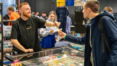 Standhouder overhandigt een trading card aan een bezoeker op een CollectableWorld TCG-beurs
