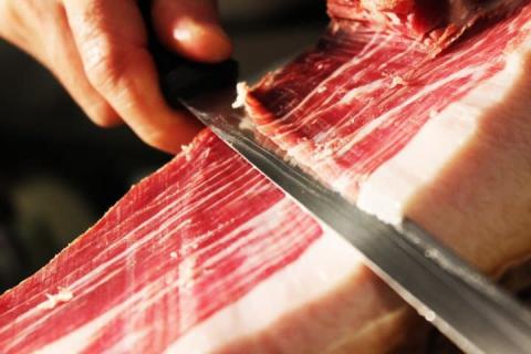 Slager Spijkenisse is bezig met het snijden van een groot stuk parmaham