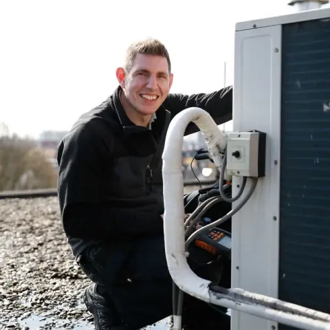 Een man in een zwart jasje werkt aan een airconditioner
