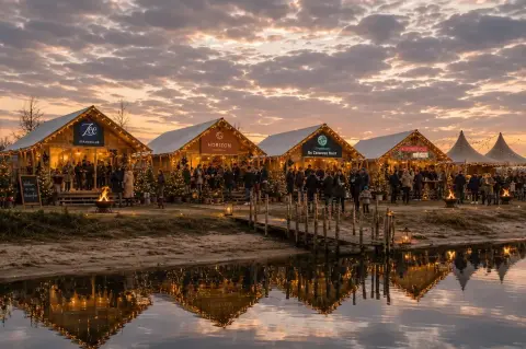 Bezoekers bij de verlichte winterfair-stands en vuurkorven aan het water bij schemering