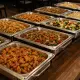 Een rij warmhouders met onder andere bami, nasi, gewokt rundvlees, gefrituurde kip en groenten