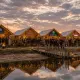 Bezoekers bij de verlichte winterfair-stands en vuurkorven aan het water bij schemering