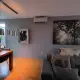 Moderne woonkamer met grijze muren, houten vloer, een Daikin Stylish airco aan de muur, een grote zwart-wit wandfoto van een bos, een grijze hoekbank en een houten eettafel met hanglampen en decoraties.